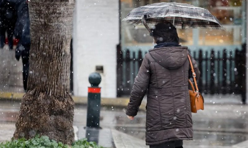 γυναίκα περπατάεισ τον δρόμο κρατώντας ομπρέλα ενώ ριχνει χιονι